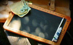 Alte Schultafel zum Schreiben am Tisch, mit Buchstaben auf dem Holz außenrum, einem kleinen gehäkelten Schwamm und einer Kreide